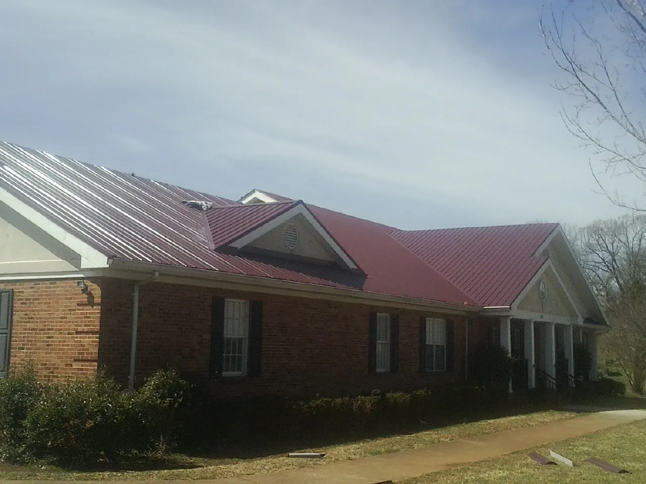 Red metal roof with gabled entries on a long brick building, from a Hail Damage Roof Repair job in Chatham